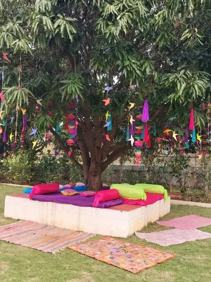 A playful and colorful Mehendi seating area under a tree. We used bright cushions and hanging fabric tassels to create a relaxed, bohemian-inspired nook for guests.