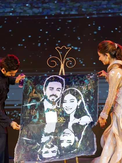 The couple revealing a glitter painting of their portrait on stage. This is a fantastic entertainment element for a sangeet or reception that wows the guests and leaves the couple with a unique memento.