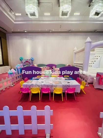 A wide view of a complete kids' zone, featuring our pastel play area, a white bouncy castle, and a long table with colorful chairs for activities.