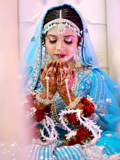 A serene moment during a Nikkah ceremony. The bride's hands are raised in prayer, showcasing her intricate henna and the stunning silver and blue jewelry.