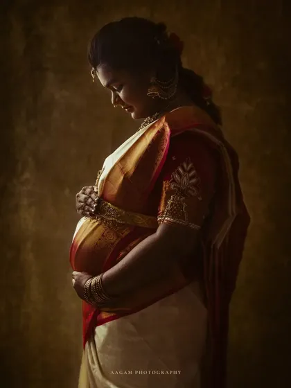 A quiet, contemplative portrait of a mother-to-be in a traditional silk saree. The lighting is soft and painterly, honoring her heritage with grace.
