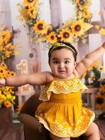 A bright and happy portrait from a sunflower-themed first birthday session, with the baby girl reaching out with a cheerful expression.