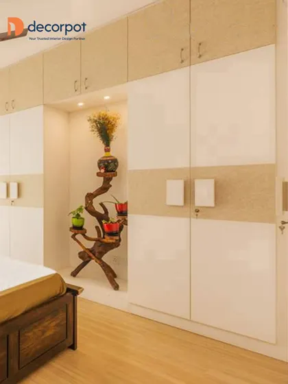 This elegant hinged wardrobe combines white laminate doors with a textured beige accent. The design includes a beautiful open niche to display a decorative plant arrangement, adding a natural touch.