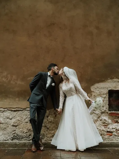 A tender kiss against a textured wall, capturing a moment of private affection during their public celebration.