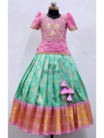 An elegant pattu pavadai with a pink peplum top and a sea-green Banarasi skirt. The top features beautiful gold and pink maggam work.