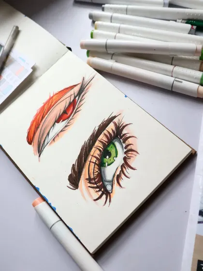 A sketchbook page with two different eye studies. I was experimenting with a more stylized, anime-like look using markers, focusing on vibrant colors and bold lashes.