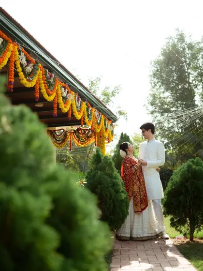 The couple stands in front of their home, decorated with marigolds for the wedding festivities. A beautiful portrait that feels personal and intimate.