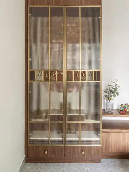 The closed view of the puja unit, showcasing the elegant fluted glass and brass-finished metal frame. The design allows for the sacred space to be discreetly tucked away when not in use.