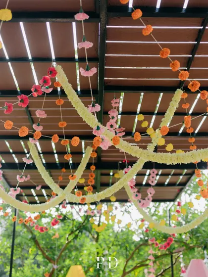 A ceiling of colorful marigold and tuberose garlands, creating a festive and traditional canopy for a Mehendi ceremony.