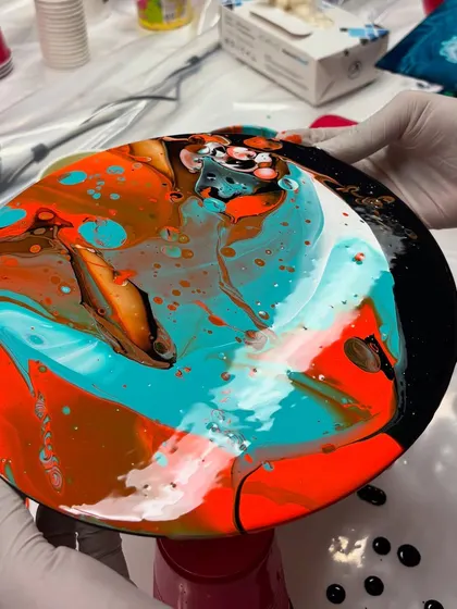 A participant holding up their freshly poured fluid art creation. The combination of orange, turquoise, and black came out so beautifully in this piece.