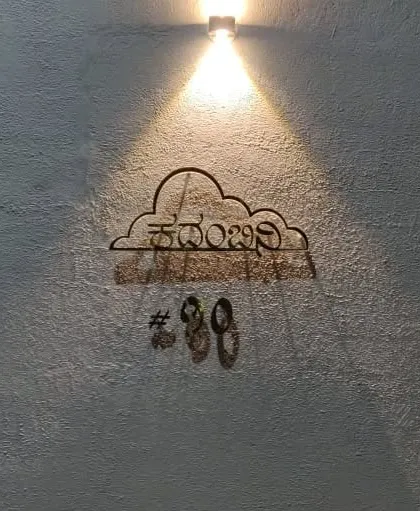 At night, the custom nameplate is highlighted by a single spotlight, casting beautiful shadows and emphasizing the texture of the compound wall.