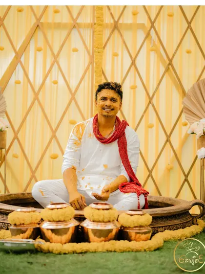 The groom smiling after the Haldi rituals, seated in front of traditional copper pots.