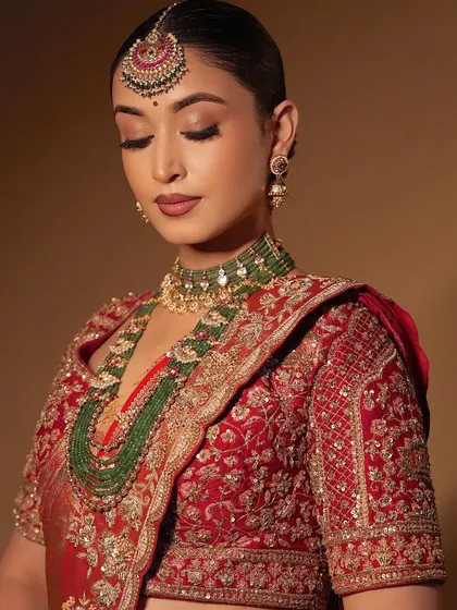 The complete look, showcasing the beautiful red lehenga and green jewellery. The makeup ties everything together, creating a look of pure elegance.