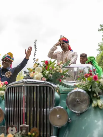 Here comes the groom. This vibrant shot captures the energy of the Baraat, with a vintage car, colorful smoke, and the groom's happy salute to his guests.