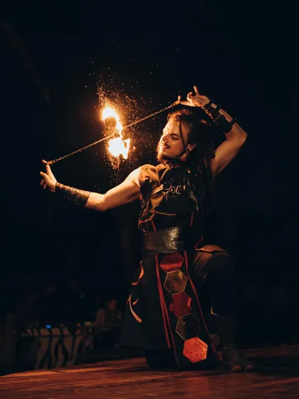 A male fire performer kneels while spinning a fire poi, creating a shower of sparks. This shot highlights the spiritual and focused nature of our fire art.