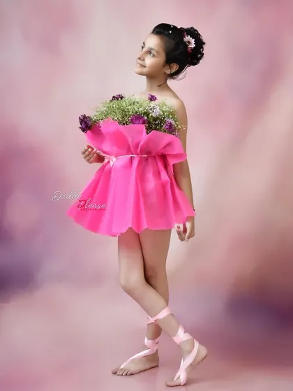 An elegant portrait of a girl in a pink dress made from flowers, holding a bouquet. Her upward gaze and the soft, painterly background give the photo an artistic quality.