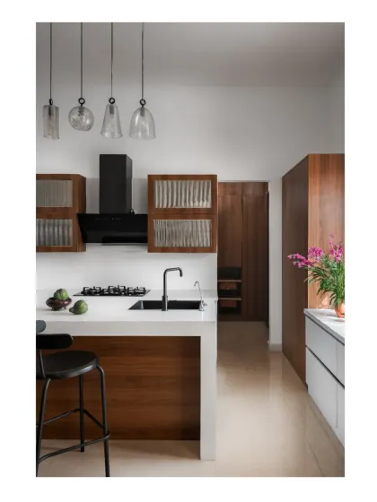 The kitchen in the Hemadri penthouse combines warm wood, crisp white countertops, and fluted glass cabinets for a look that is both minimal and textured.