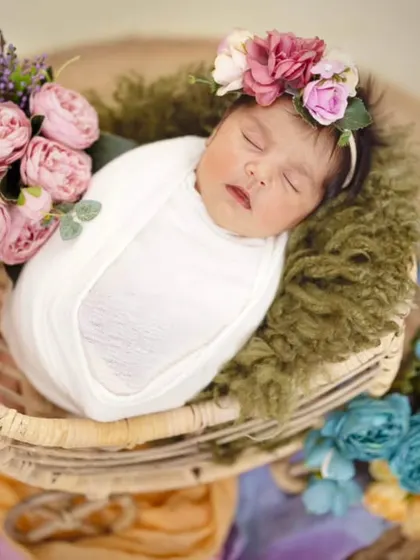 A sweet 22-day-old baby girl sleeping peacefully in a carry cart. The arrangement of soft flowers around her adds a dreamy, delicate touch to this newborn portrait.