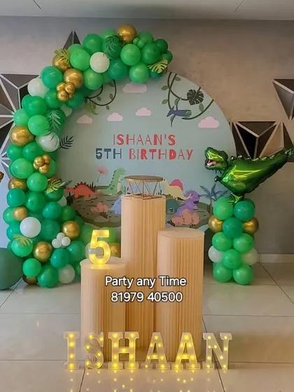 A roaring dinosaur theme for a 5th birthday, featuring a custom backdrop, a green and gold balloon arch, and dinosaur foil balloons.