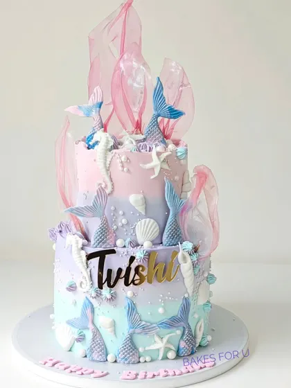 An underwater fantasy, this two-tier mermaid cake is decorated in pastel shades of pink, purple, and blue. It features mermaid tails, seahorses, and delicate rice paper sails for a dreamy, oceanic feel.