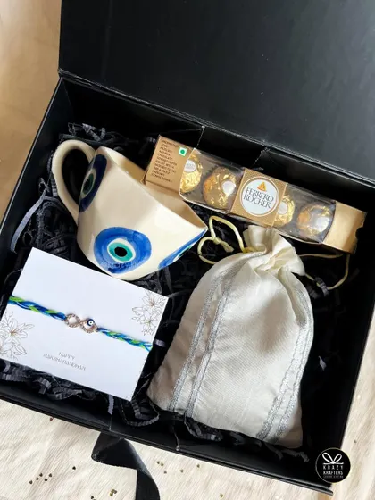 The 'Raksha' hamper, a simple yet powerful gift with an evil eye mug, an infinity rakhi, and sweet treats.