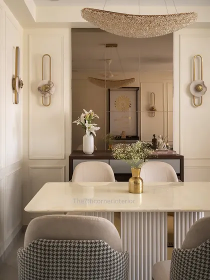 This image captures the blend of modern elegance and timeless charm in the dining area. Muted tones, gold accents from the wall sconces and vase, and soft textures create a serene dining experience.