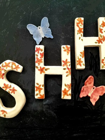 Custom handmade ceramic letters, perfect for personalizing a room. These letters are painted with delicate orange flowers and are accompanied by a few ceramic butterflies for a whimsical touch.