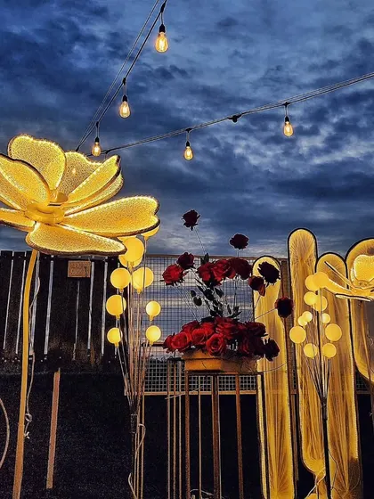 An artistic shot of the large, illuminated flower props against a dramatic evening sky, part of a romantic rooftop setup.
