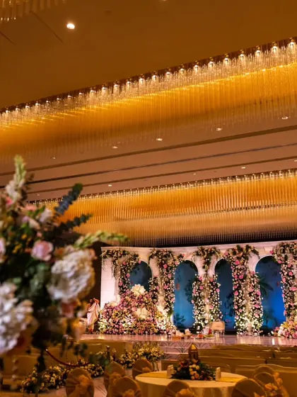 A view of the grand reception stage from a guest's perspective. The combination of the magnificent floral backdrop and the opulent crystal chandeliers of the venue created a truly spectacular sight.