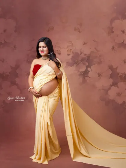 This bare-bump saree drape is a beautiful way to celebrate the female form during pregnancy. The soft, painterly background adds a touch of artistic elegance.