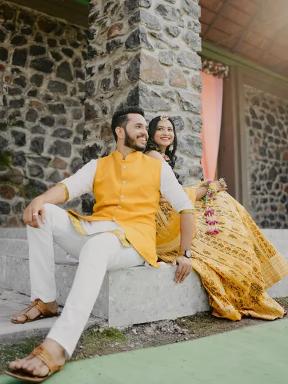 A relaxed and happy portrait of a couple during their Haldi ceremony. Dressed in shades of yellow and white, they share a candid moment on the steps.