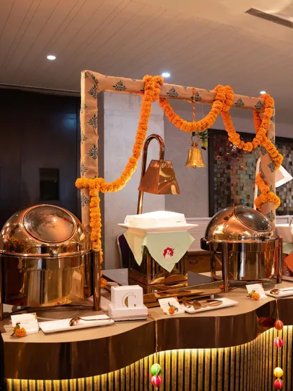 A traditional buffet station adorned with marigold garlands and brass bells. The gleaming copper chafing dishes add a touch of royalty to the setup, reflecting our commitment to heritage.