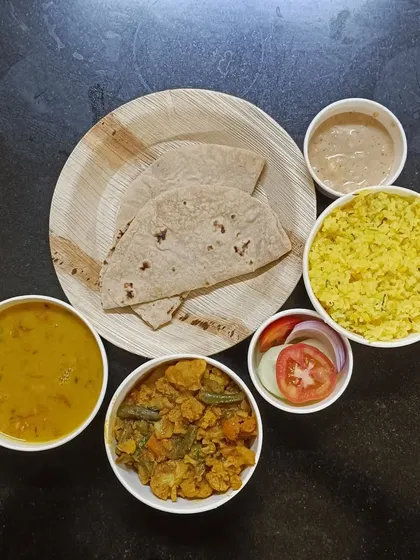 A single trial meal plate, showing a complete portion. It includes lemon rice, mixed vegetable sabzi, dal, two rotis, salad, and a side of dessert. It’s a perfect preview of what we offer.