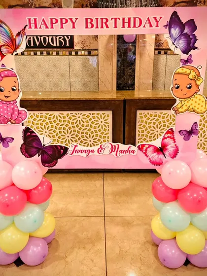 A fun photo booth frame for Inaaya and Manha's twin birthday party. The butterfly and baby-themed frame is supported by colorful balloon columns.