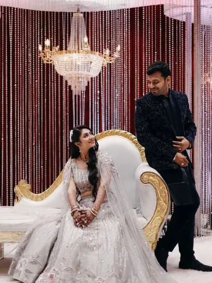 A romantic pose on a glamorous reception stage. The decor features a stunning crystal chandelier and a backdrop of shimmering bead curtains, creating a sophisticated and sparkling setting for the couple.