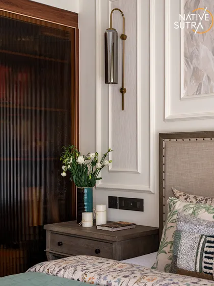 A detail shot of the bedside, highlighting the fluted glass wardrobe, elegant wall sconce, and classic wall paneling. This composition of textures and materials demonstrates our meticulous attention to detail.