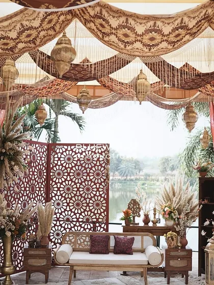 The serene lakeside seating for a Dubai Souk-themed Mehendi, featuring rustic furniture, pampas grass, and intricate jaali screens.
