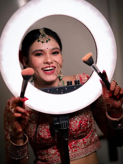 A fun and playful bridal portrait where the bride smiles brightly while posing with a ring light and makeup brushes. This shot captures her joyful personality and the excitement of getting ready.