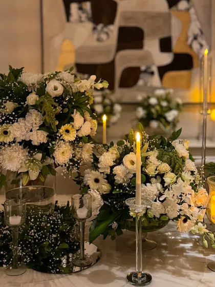 A close-up of the magnificent dining table centerpiece, showing the dense arrangement of white flowers and the warm glow of the surrounding candles.