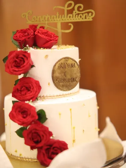 This beautiful two-tiered cake, decorated with red roses and a custom nameplate, is topped with a "Congratulations" sign. It's a perfect centerpiece for an engagement or anniversary celebration.