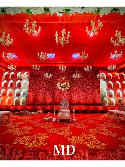 The central seating for the couple at their engagement ceremony. The ornate silver chairs are placed on a stage covered with a royal red and gold patterned carpet, perfectly matching the 'Laal Ishq' theme.