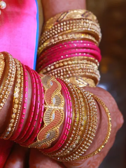 A detail shot of a bride's hands adorned with stacks of pink and gold bangles.