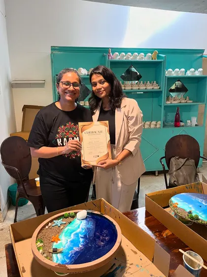 A participant proudly displays her certificate and the stunning resin ocean art piece she created.