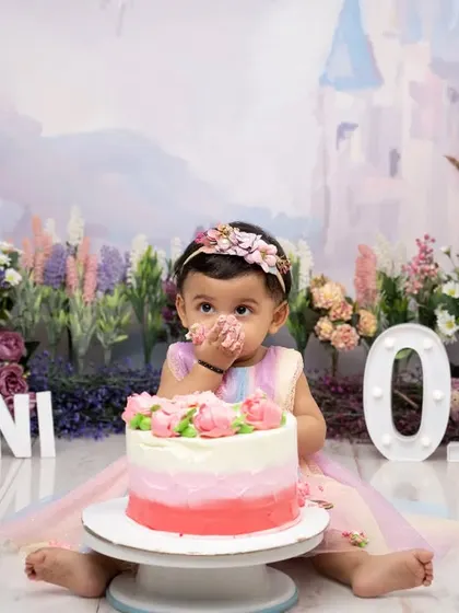 A taste of birthday magic! This little girl, dressed as a princess in a fairytale setting, gets her first taste of cake, a perfect moment captured during her "One" year photoshoot.