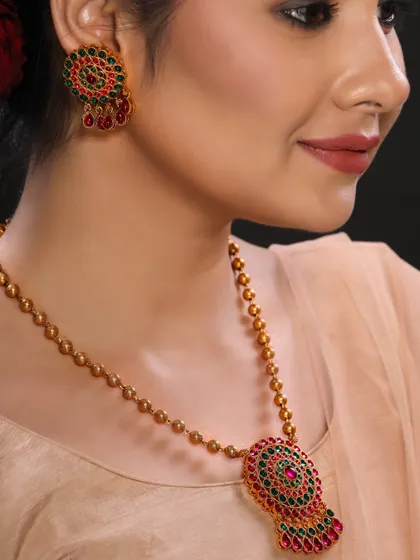 A model wearing a traditional gold necklace with red and green stones, perfect for a classic ethnic jewellery catalogue.