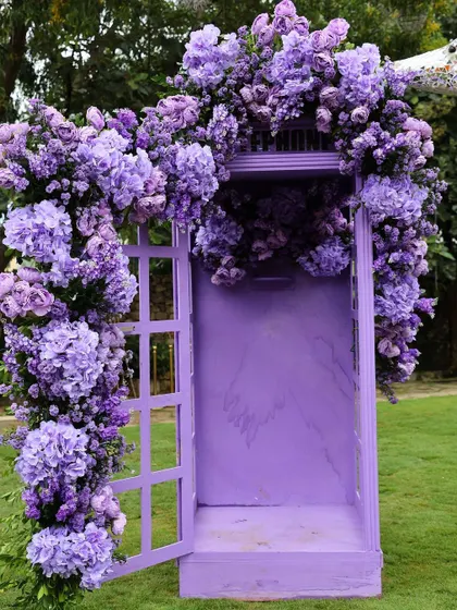 A whimsical purple telephone booth covered in a cascade of purple flowers, serving as a unique and interactive photo installation.