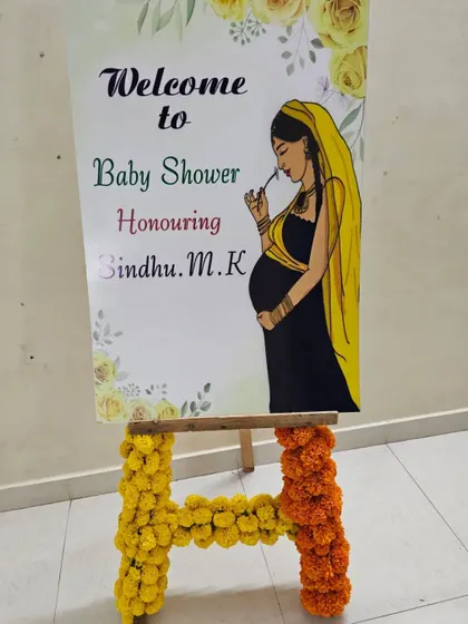 A personalized welcome sign for a baby shower, honoring Sindhu. The easel is decorated with marigold flowers to match the traditional theme.