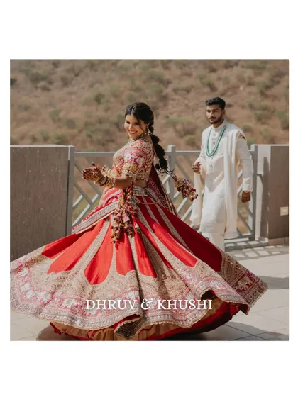 A joyful twirl from the bride on her wedding day. This dynamic shot captures her happiness and the beautiful movement of her red lehenga, with the groom looking on in the background.