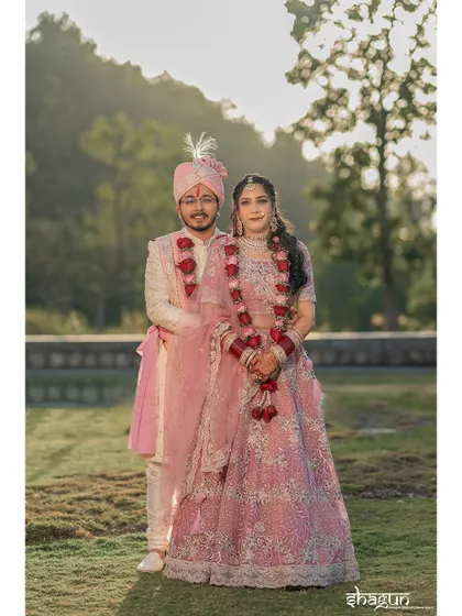 A beautiful outdoor portrait of the couple in matching pink outfits, surrounded by the lush greenery of their wedding venue.