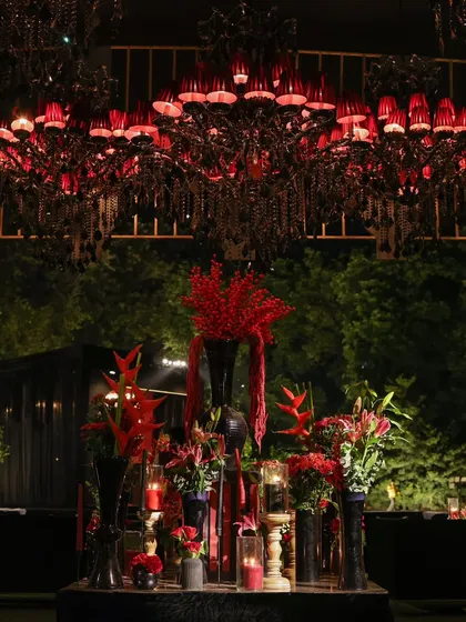 A magnificent red-shaded chandelier serves as a centerpiece, casting a warm, dramatic glow over an artfully arranged display of red flowers and decor elements.